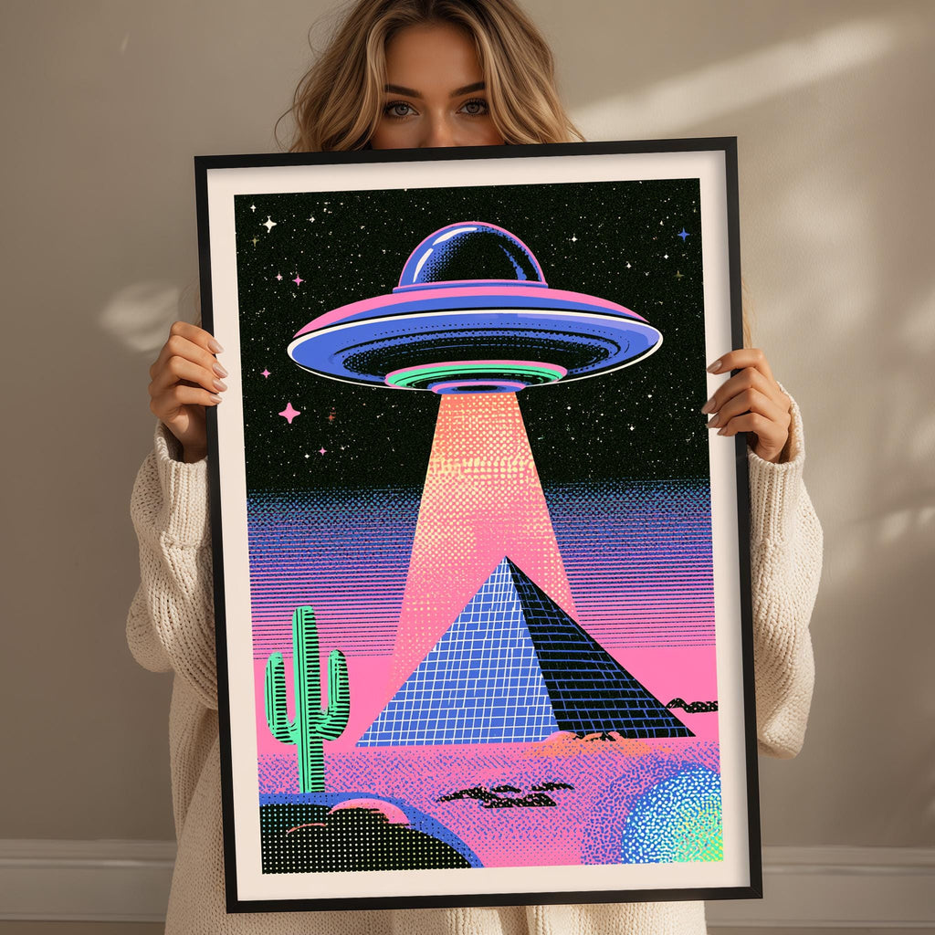 A woman holds up a framed poster depicting a surreal scene with a large alien spacecraft hovering over a desert landscape, including a cactus and a pyramid.