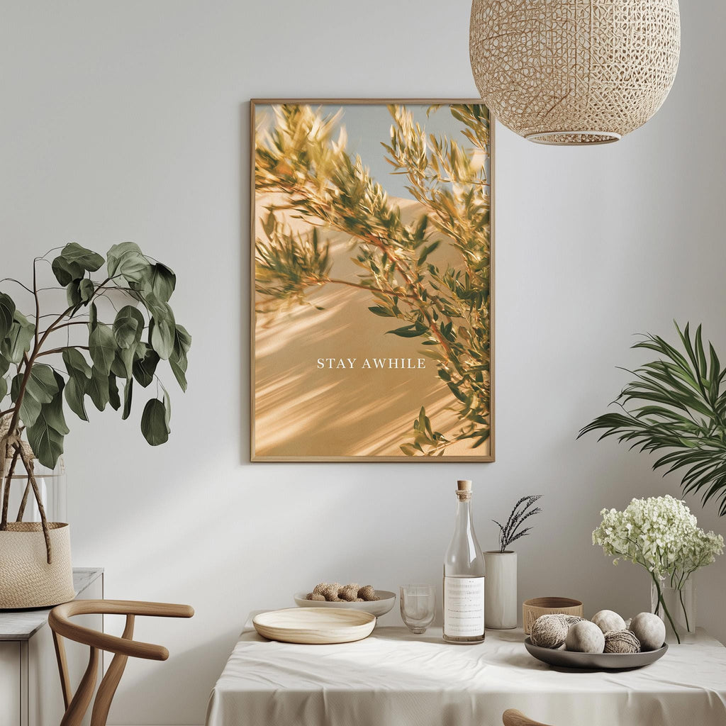 a dining table with a bowl of fruit, a bottle, and a vase of flowers, along with a framed picture hanging on the wall above the table.