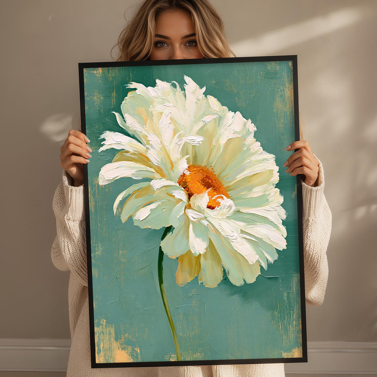 A woman holds a framed painting of a large white flower with an orange center, standing in front of a green background.