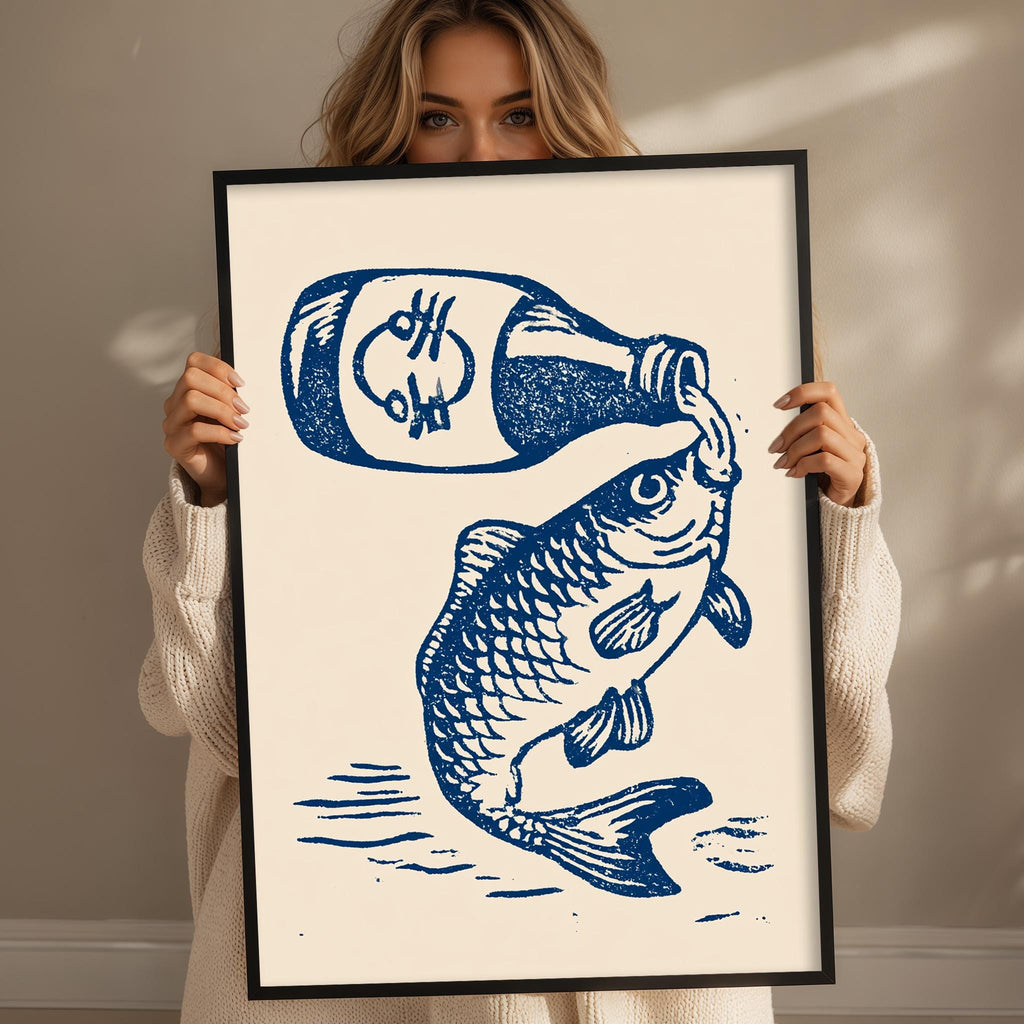 A woman is holding up a framed print that features a fish and a bottle of something, likely a drink.