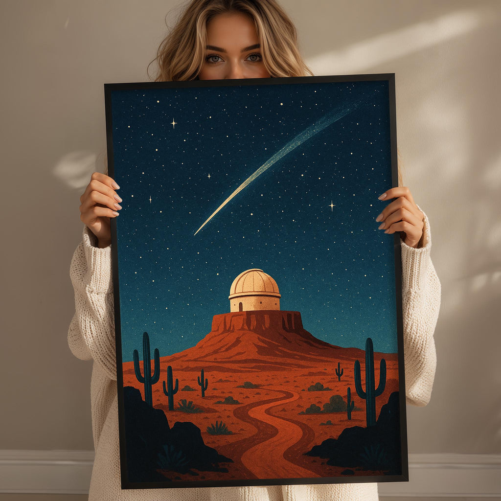 A woman holds up a framed illustration depicting a desert landscape with a large dome-shaped structure, cacti, and a starry night sky.