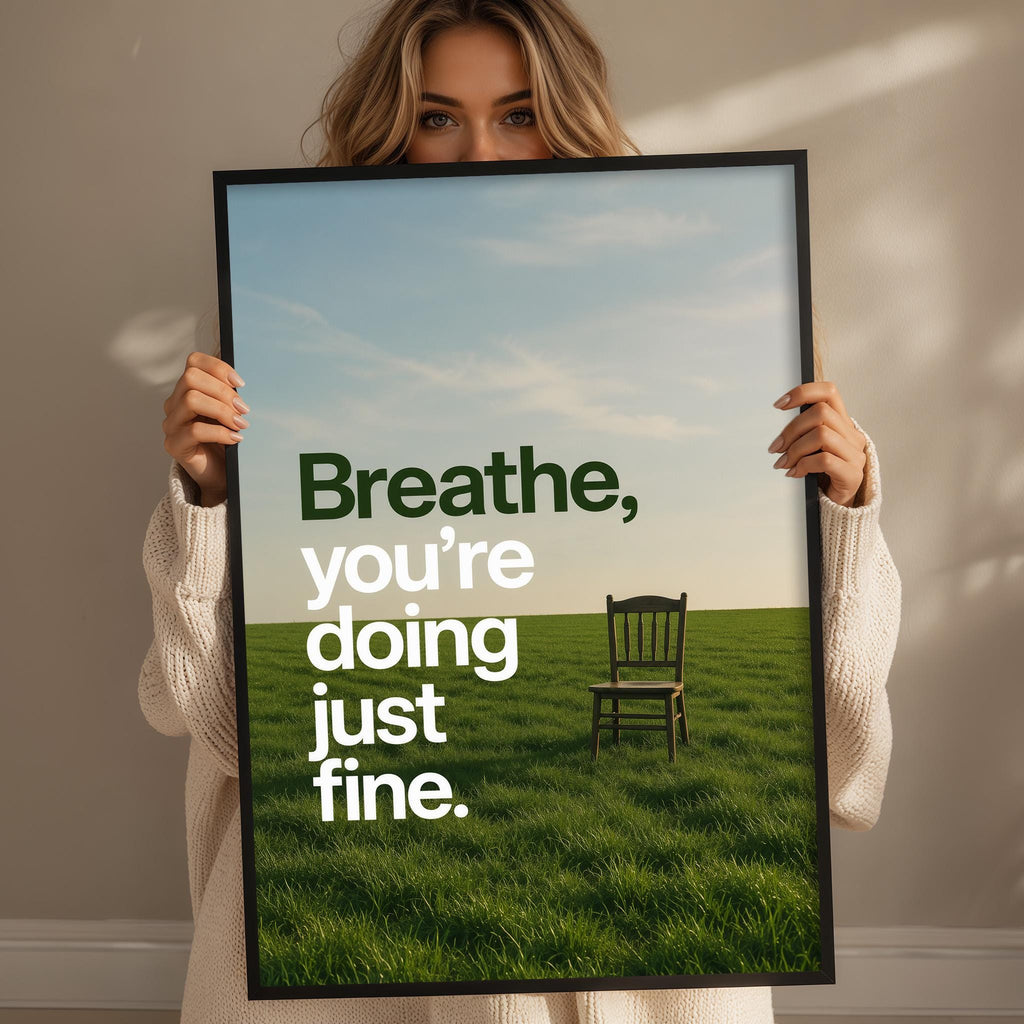 A woman holding a framed poster with a serene image of a chair in a grassy field, along with the text "Breathe, you're doing just fine."