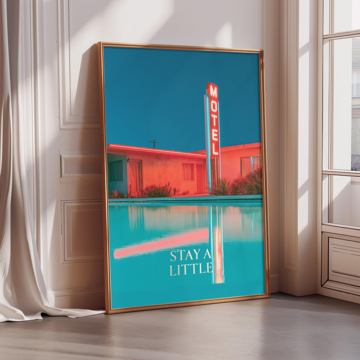 A framed poster of a motel with a bright blue sky and a pool in the foreground, with the text "STAY A LITTLE" displayed on the poster.