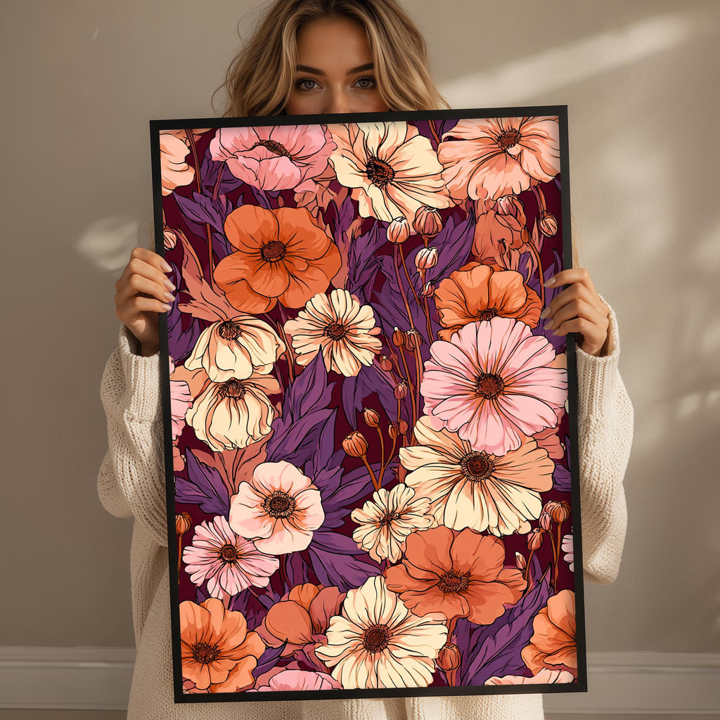 A woman is holding up a framed print of a vibrant floral pattern with various shades of orange, pink, and purple flowers.