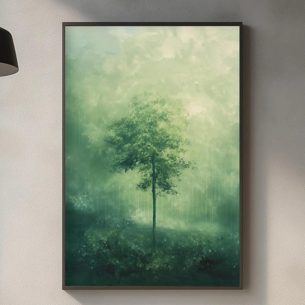 a kitchen counter with a framed painting of a tree in a misty forest scene hanging above it. The kitchen counter also has various kitchen items such as a cutting board, a bottle, and a vase.