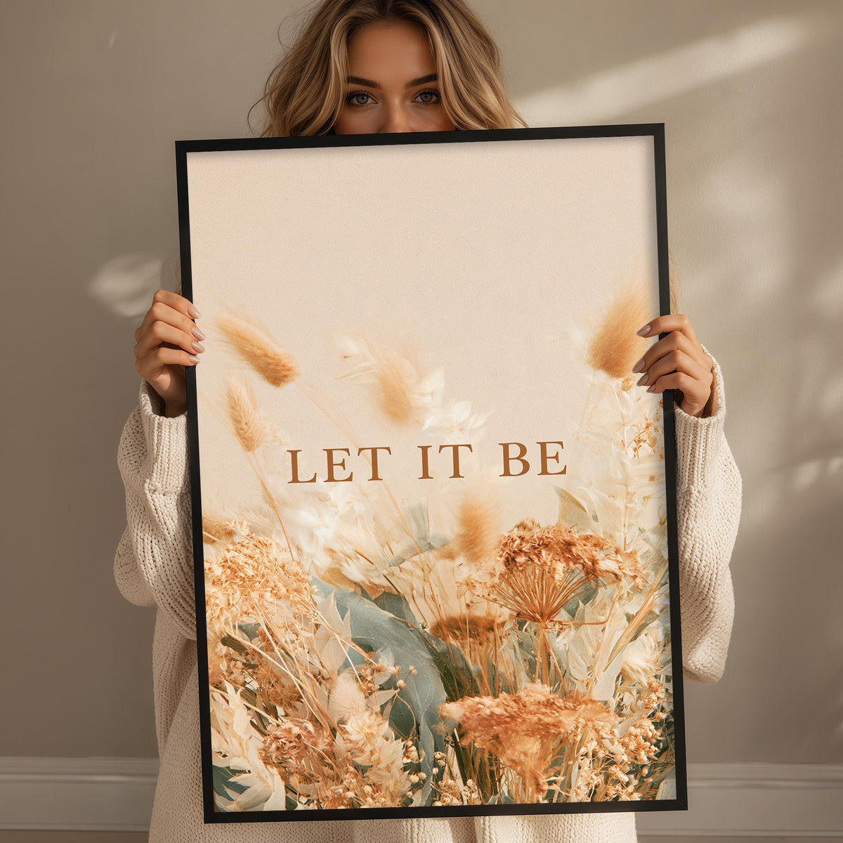 A woman holding a framed print with a floral design and the text "LET IT BE" on it.