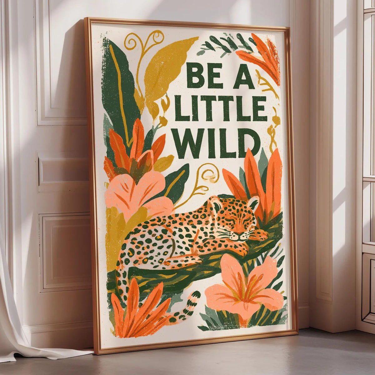 A framed poster with a leopard and tropical plants, featuring the text "Be a little wild".