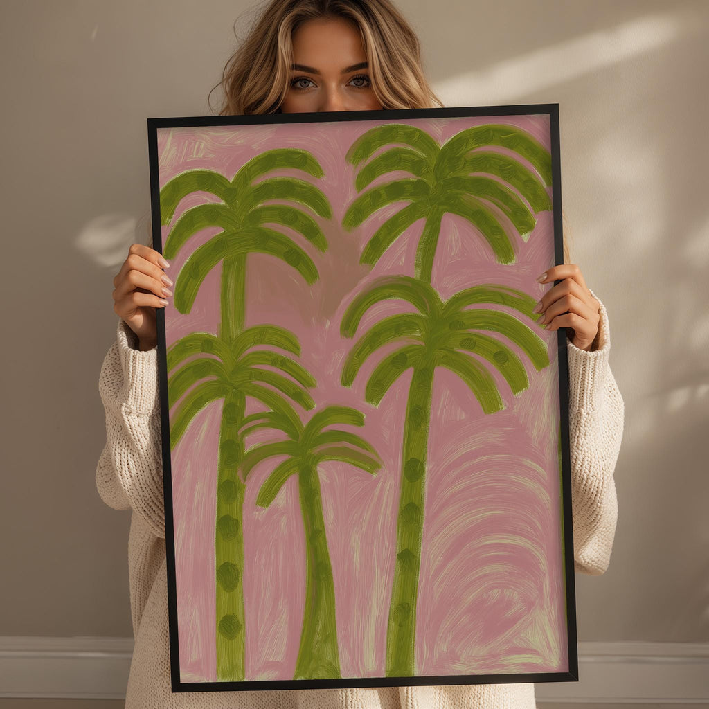A woman holding a framed painting of palm trees in front of her face.
