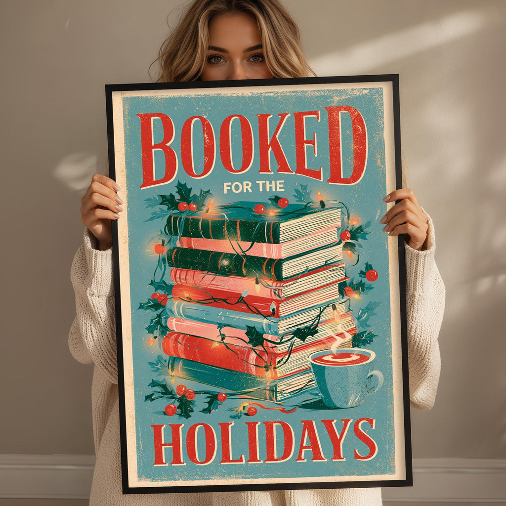 A woman is holding up a framed poster with the text "BOOKED FOR THE HOLIDAYS" and an illustration of a stack of books with Christmas lights and a cup of hot chocolate.