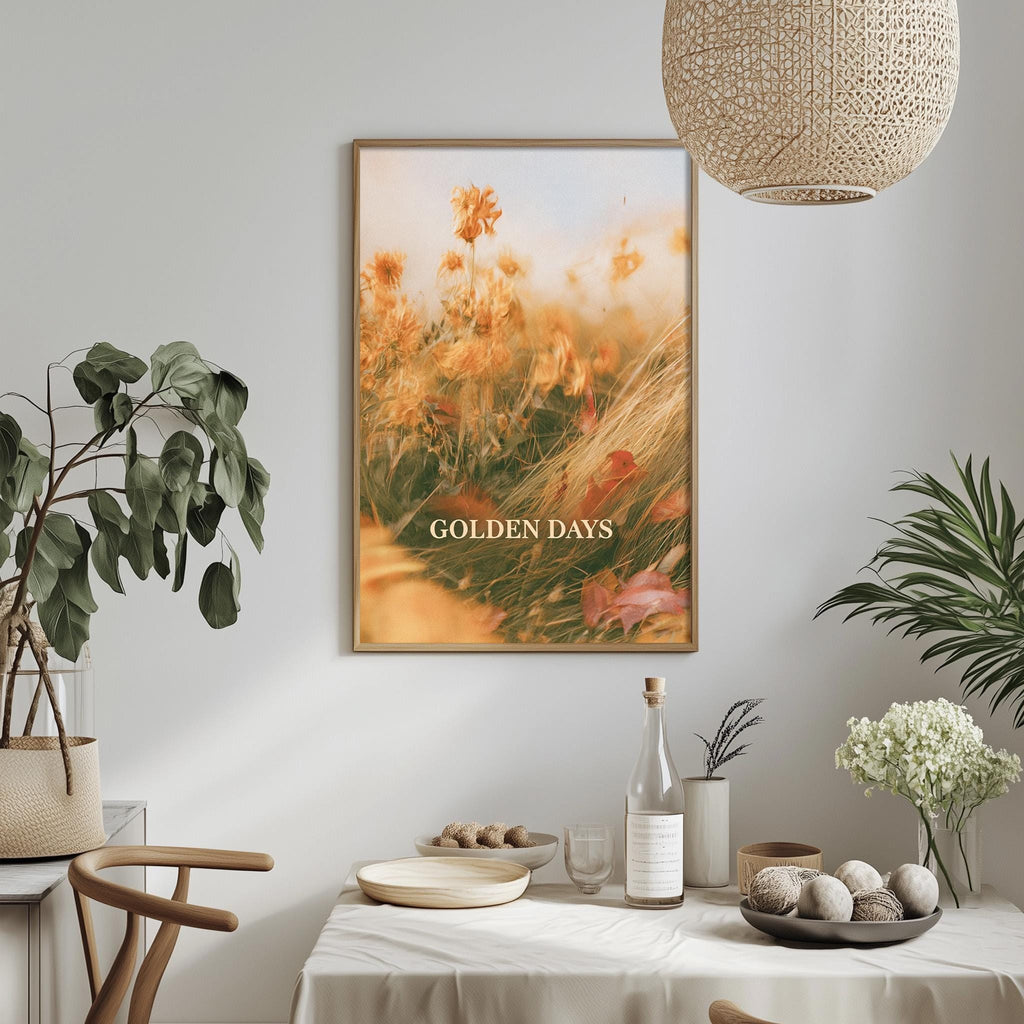 a dining table set with a white tablecloth, a bowl of fruit, a bottle, and a vase with flowers. Above the table, there is a framed picture of a field with flowers, and a hanging light fixture.