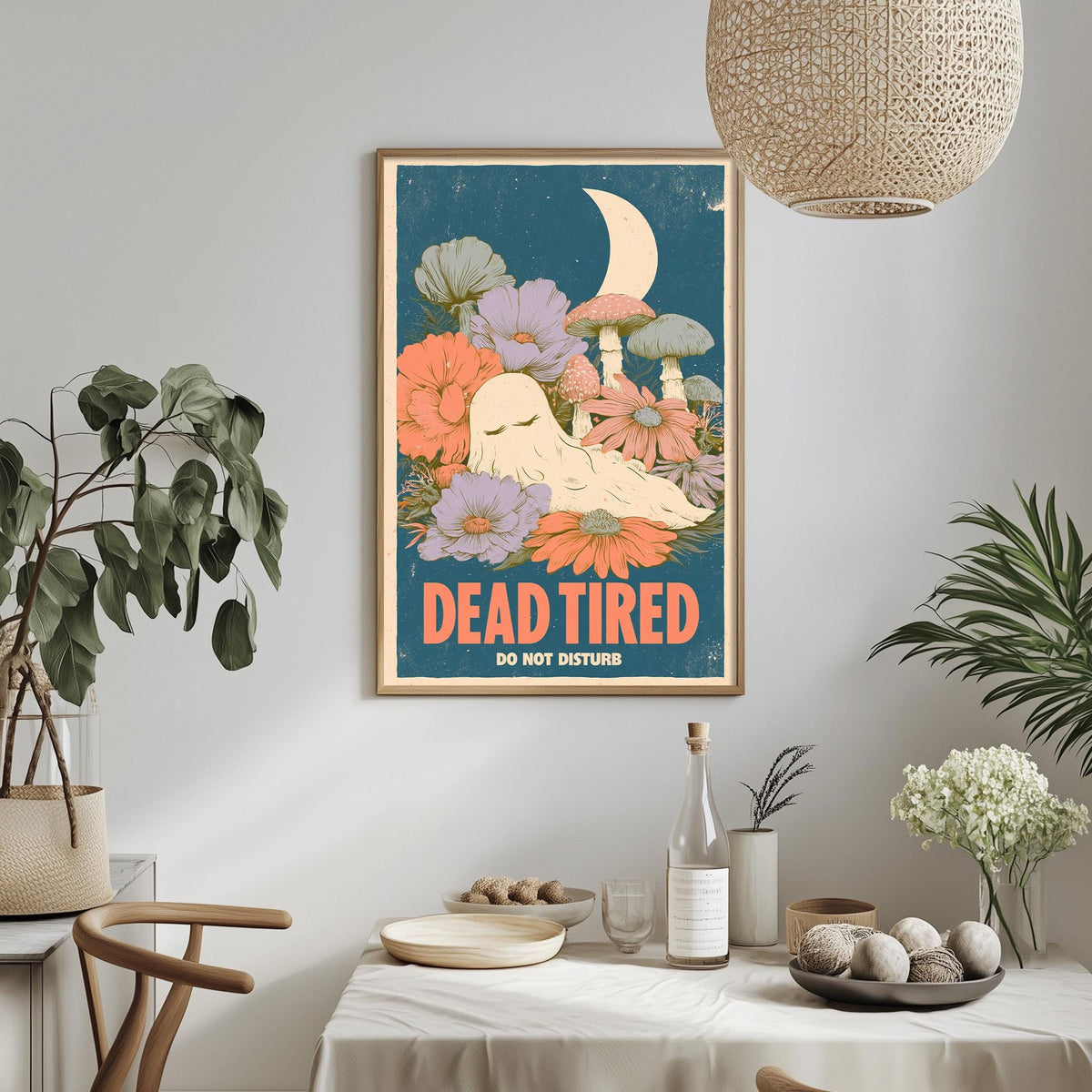 a framed poster with a whimsical illustration of a sleeping ghost surrounded by flowers and mushrooms, hanging on a wall above a dining table with various decorative items.