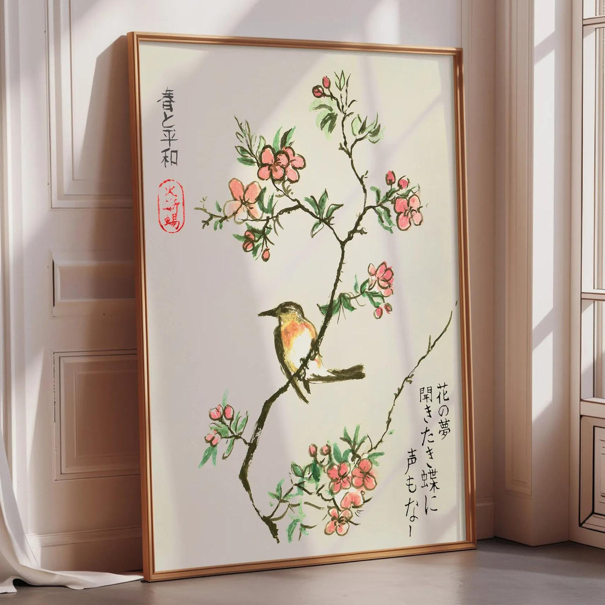 A framed painting depicting a bird perched on a branch with pink flowers, placed on a wooden floor in a room with a window.