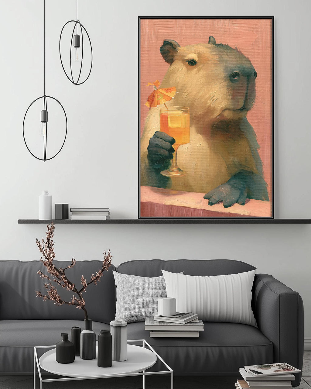 a large painting of a capybara holding a glass of orange juice, hanging on a wall above a gray couch with a coffee table in front of it.
