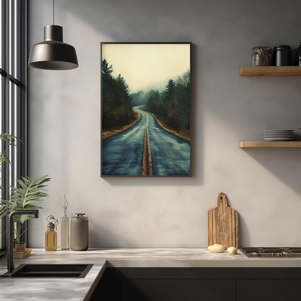 a kitchen counter with various kitchen items, including a cutting board, a bottle, and a vase. Above the counter, there is a framed picture of a winding road through a forest, creating a serene and natural atmosphere in the kitchen.
