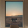 a modern and minimalist office space with a large window that offers a view of a desert landscape at sunset. The office features a wooden desk, a comfortable-looking chair, and a large framed picture of a desert scene. The room is well-lit, with a pendant light hanging above the desk and a bookshelf filled with books and decorative items.