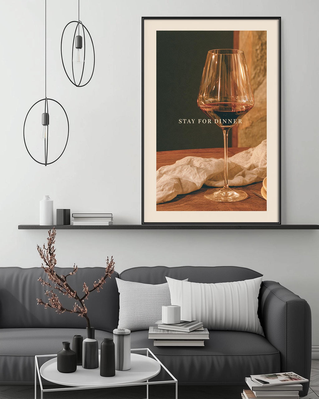 a modern living room with a gray sofa, a coffee table, and a framed poster on the wall. The poster displays a wine glass and the text "STAY FOR DINNER".