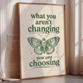 A framed poster with the text "what you aren't changing, you are choosing" and an illustration of a butterfly.