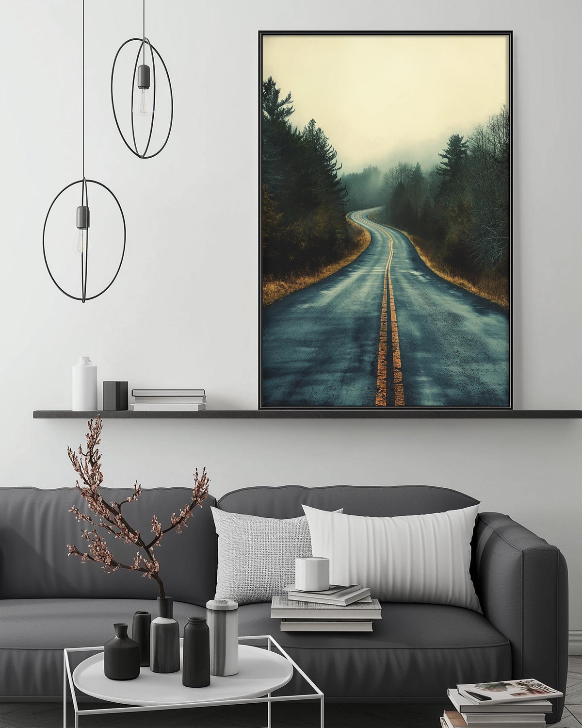 a living room with a gray sofa, a coffee table, and a large framed picture of a winding road through a forest. The room has a minimalist and modern design, with a black and white color scheme and a few decorative elements such as a potted plant and a vase.