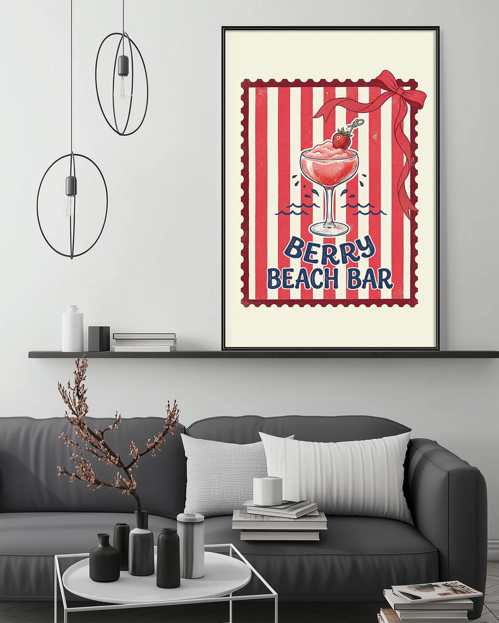 a framed poster of a berry-themed beach bar, with a glass of berry-infused drink and a red ribbon on top. The poster is displayed on a wall above a gray couch, which has a coffee table and some decorative items on it.
