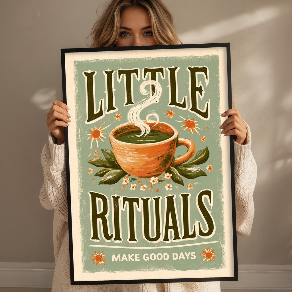 A woman holding a framed poster with a design of a cup of tea and flowers, along with the text "LITTLE RITUALS" and "MAKE GOOD DAYS".