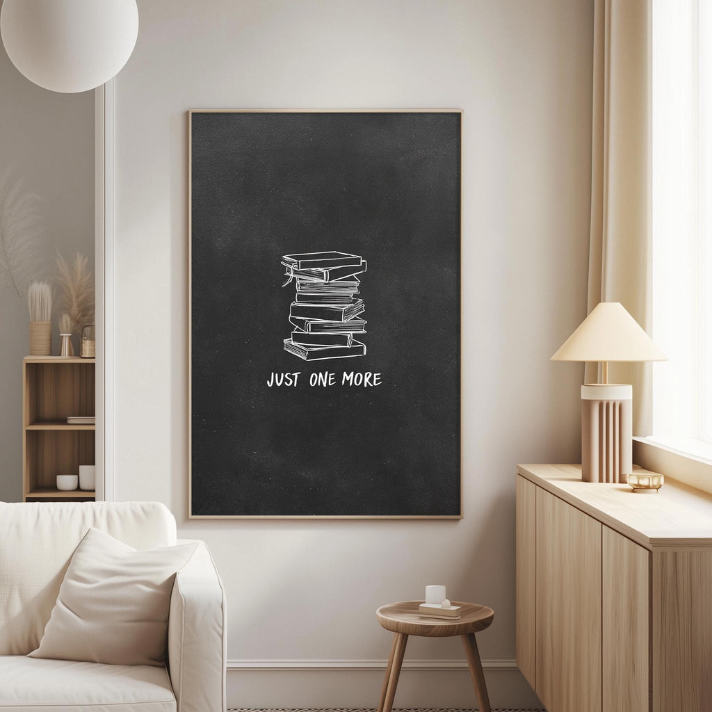 a living room with a white couch, a wooden side table, and a lamp. Above the couch, there is a blackboard with a white chalk drawing of a stack of books and the text "JUST ONE MORE" written on it.