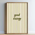 A framed poster with a striped background and the text "good energy" printed on it.