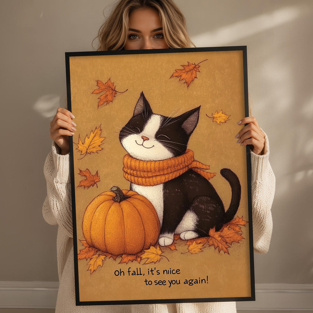 A woman holds up a framed illustration of a black and white cat sitting next to a pumpkin, surrounded by autumn leaves.