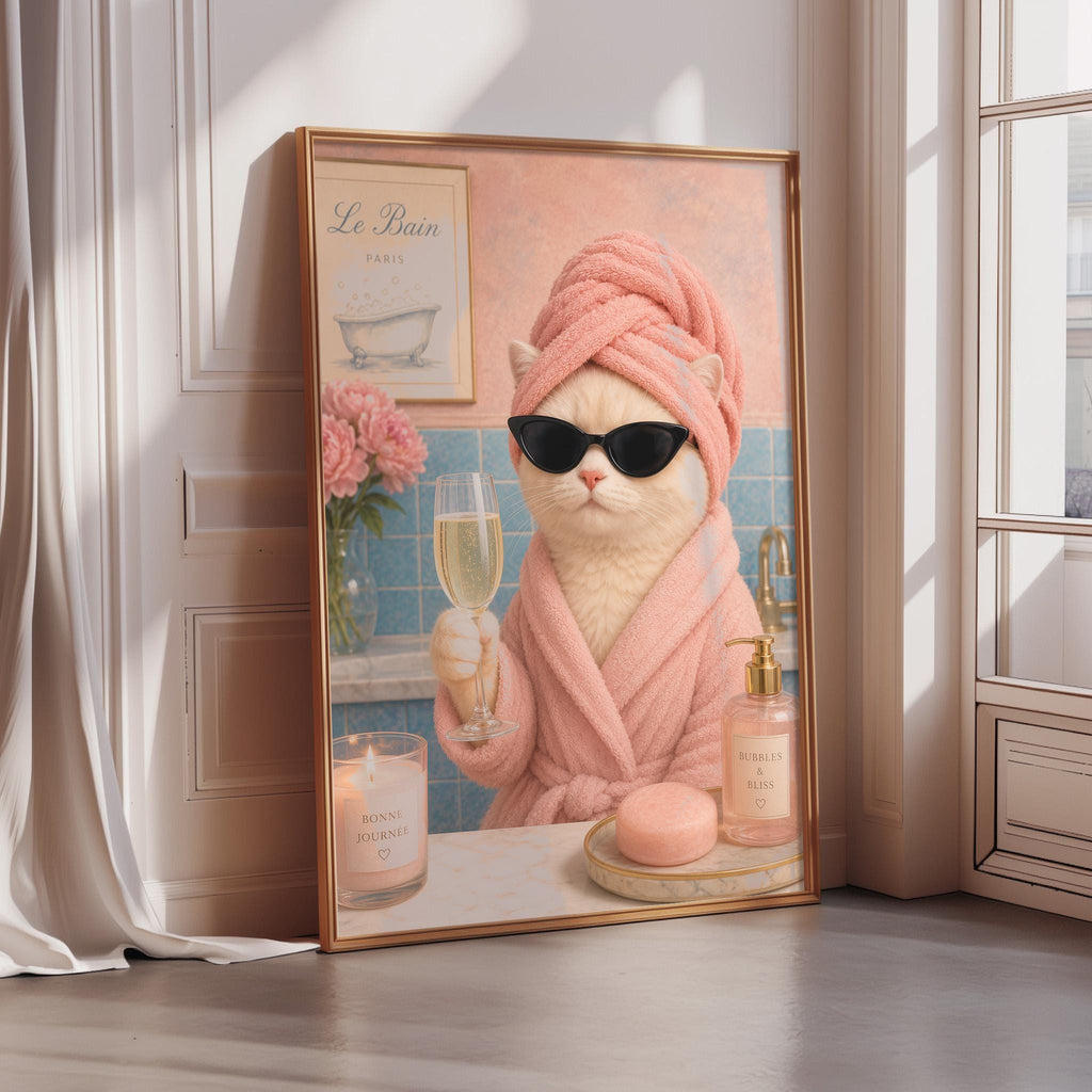 A framed illustration of a cat wearing a pink bathrobe, sunglasses, and holding a glass of champagne, with a candle and soap on a table in front of it.