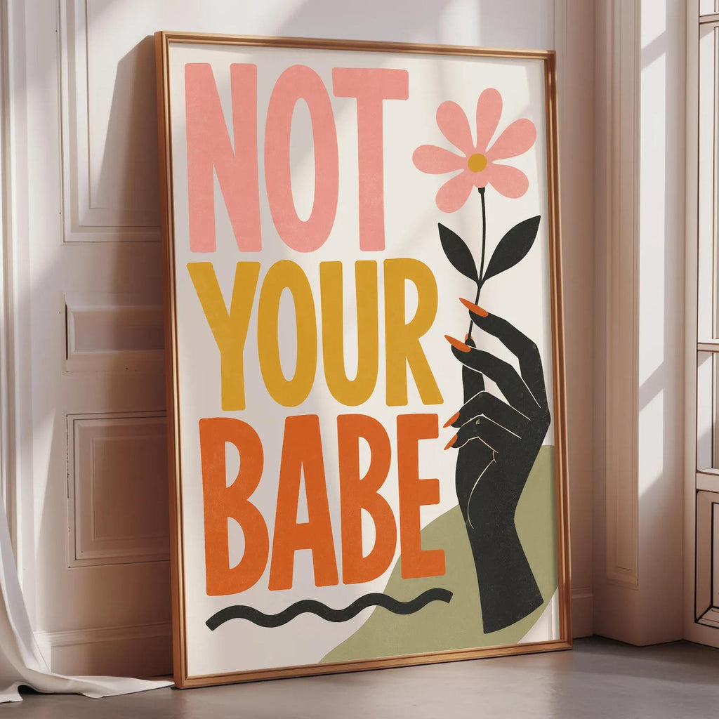 A framed poster with the text "NOT YOUR BABE" and an illustration of a hand holding a flower.