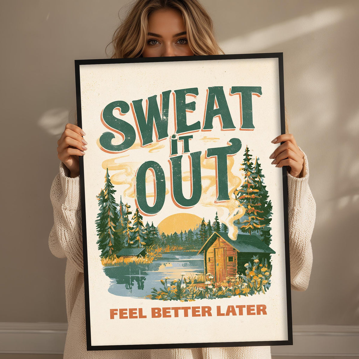 A woman holding a framed poster with a forest scene and a cabin, with the text "SWEAT IT OUT" prominently displayed.