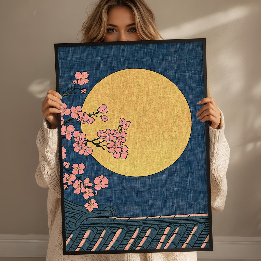 A woman holds up a framed print with a floral design and a large yellow moon.