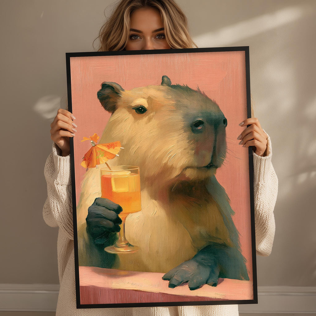 A woman holds up a framed painting depicting a capybara holding a glass of orange juice.