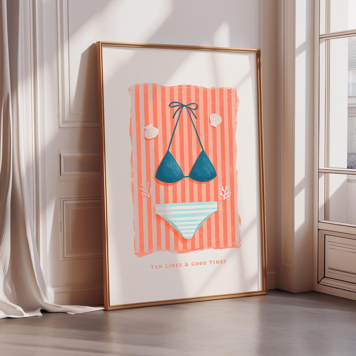 A framed poster with a beach scene, featuring a bikini top, a striped towel, and seashells, along with the text "TAN LINES & GOOD TIMES".
