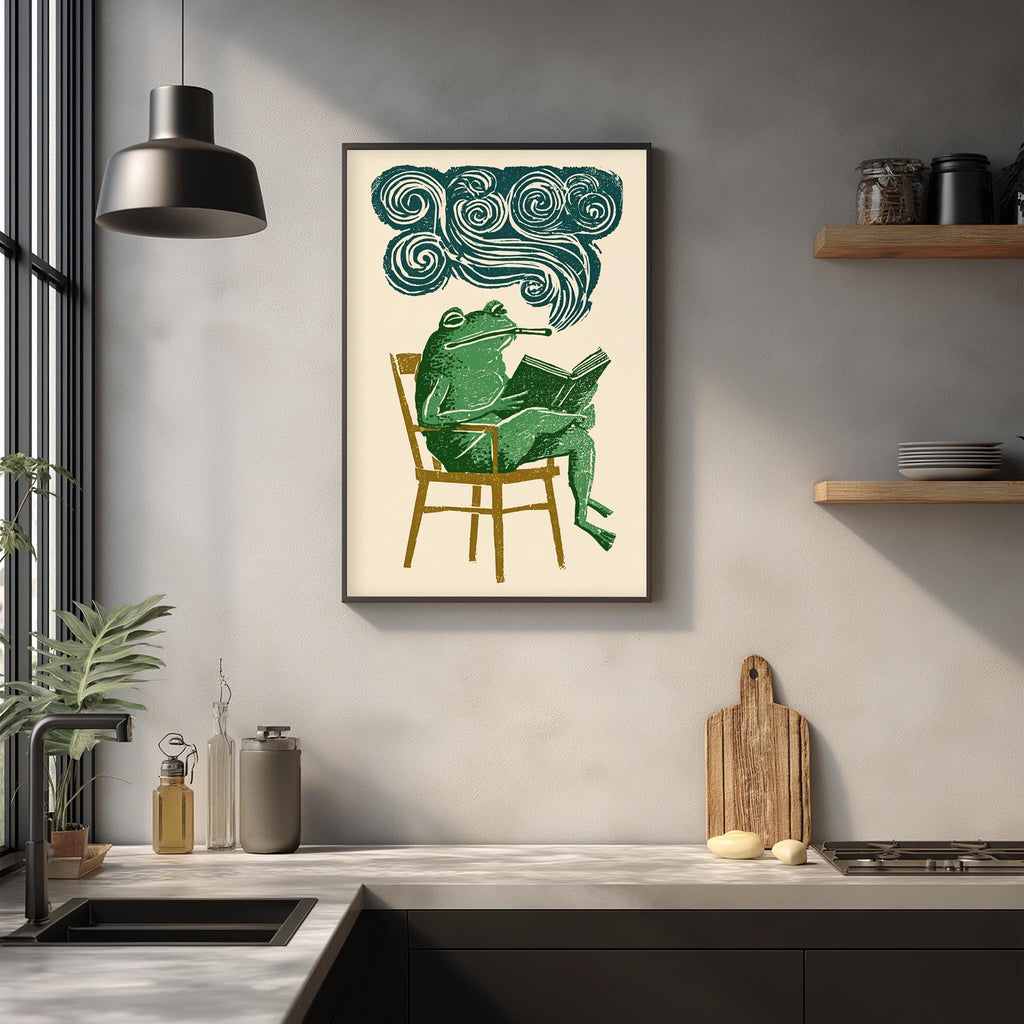a framed illustration of a green frog sitting in a chair and reading a book, with a cloud-like shape above the frog's head.