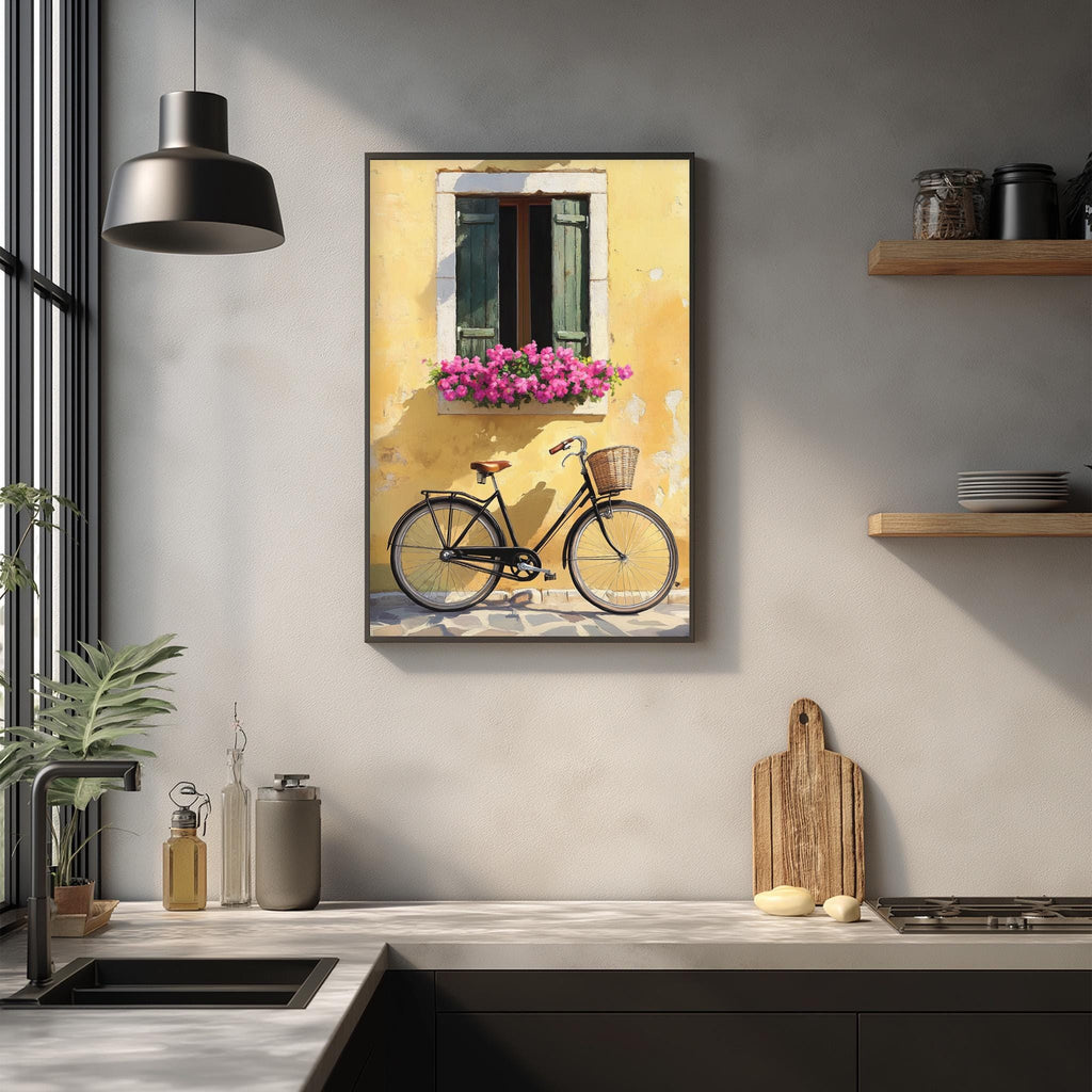 a kitchen counter with various items, including a bicycle, a plant, and a wooden cutting board. Above the counter, there is a framed picture of a yellow building with a window and pink flowers.