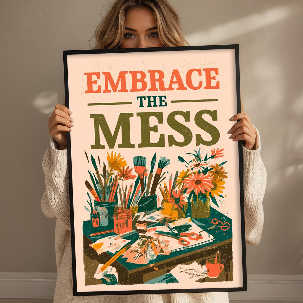 A woman holding a framed poster with the text "Embrace the mess" and an illustration of art supplies and flowers.