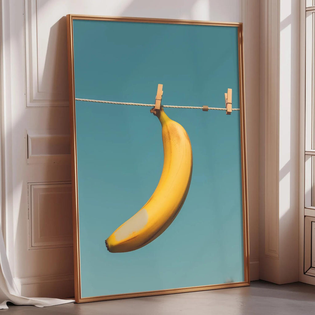 A framed image of a banana hanging on a clothesline, with a blue background.