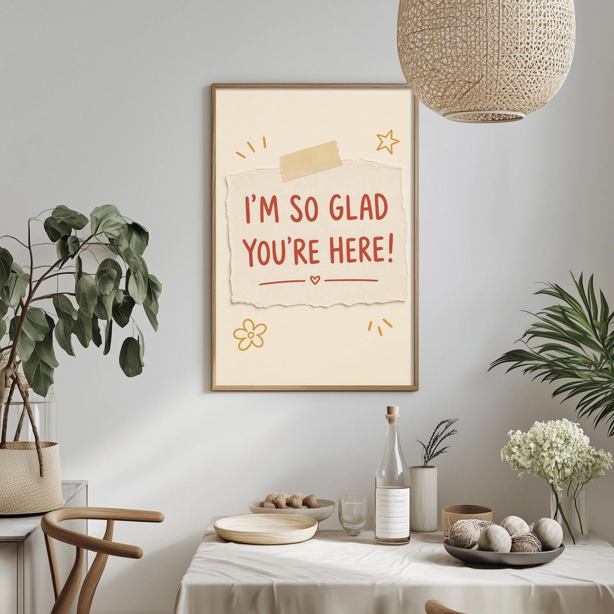 a framed poster with the text "I'm so Glad You're Here!" hanging on a wall above a dining table with various items on it, including a bottle, a bowl, and a vase.