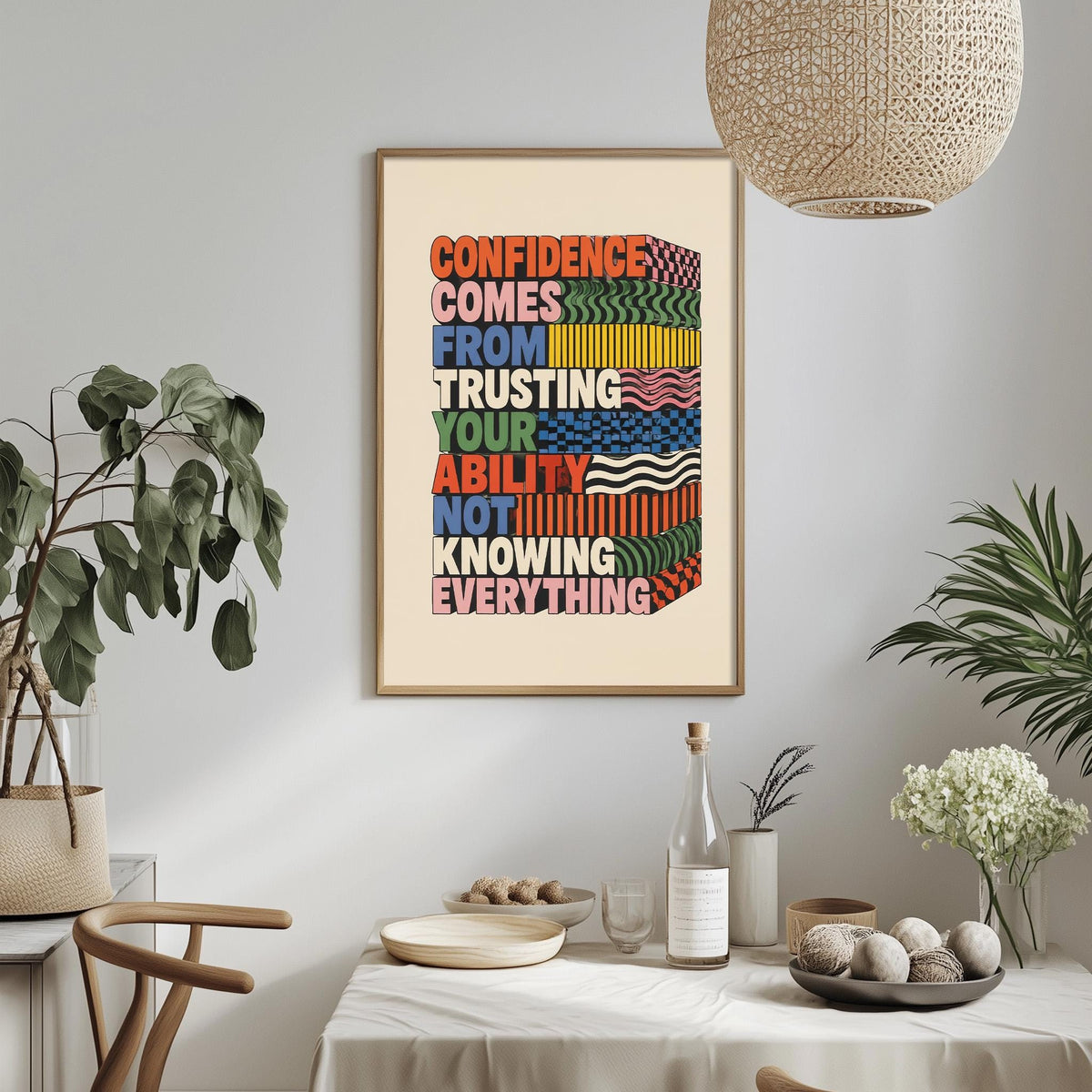 a framed motivational poster with the text "CONFIDENCE COMES FROM TRUSTING YOUR ABILITY NOT KNOWING EVERYTHING" displayed on a wall above a dining table with various items on it.