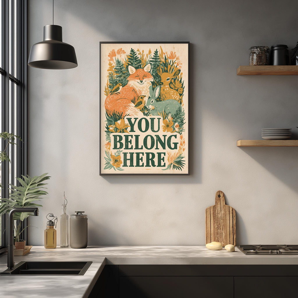 a kitchen counter with various items such as a cutting board, a soap dispenser, and a plant. Above the counter, there is a framed poster with the text "YOU BELONG HERE" and illustrations of animals, including a fox and a deer.