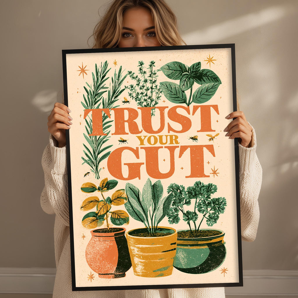A woman holding a framed poster with a colorful illustration of potted plants and the text "TRUST YOUR GUT" on it.