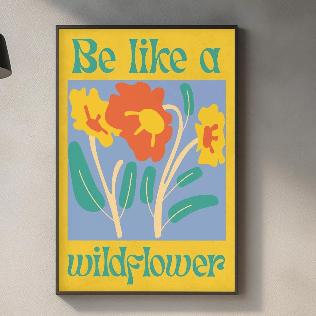 a kitchen counter with a framed poster of a wildflower design hanging above it. The poster has a yellow background with a blue border and a red flower. The kitchen counter has various items on it, including a cutting board, a soap dispenser, and a bottle.