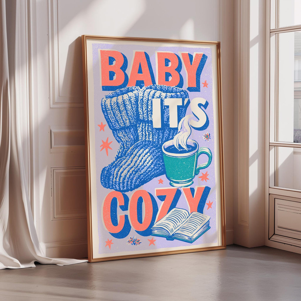 A framed poster with the text "BABY IT'S COZY" and an illustration of a pair of blue and white striped socks, a cup of hot chocolate, and an open book.