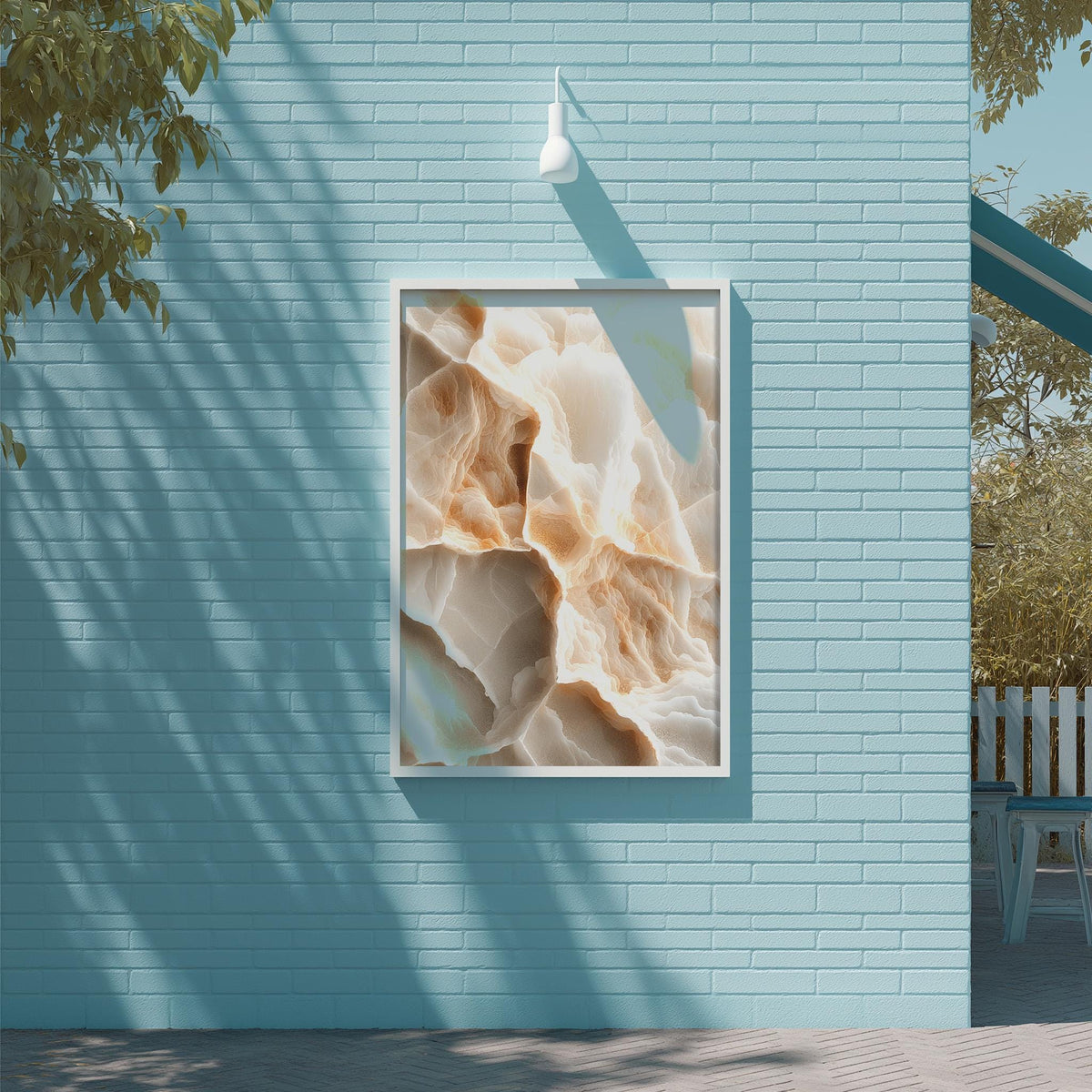 a blue brick wall with a framed abstract painting hanging on it. The painting has a textured, organic appearance with a mix of light and dark colors. The wall is situated next to a wooden deck and a tree, creating a serene and natural setting.