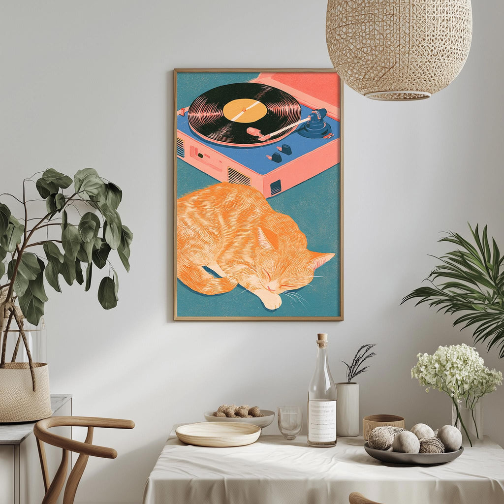 a vibrant and colorful painting of an orange cat resting on a turquoise surface, with a record player and a pink record album in the background. The painting is hung on a white wall above a dining table, which is set with various items such as a bowl, a bottle, and a vase. The table also has a potted plant and a bowl of fruit on it.