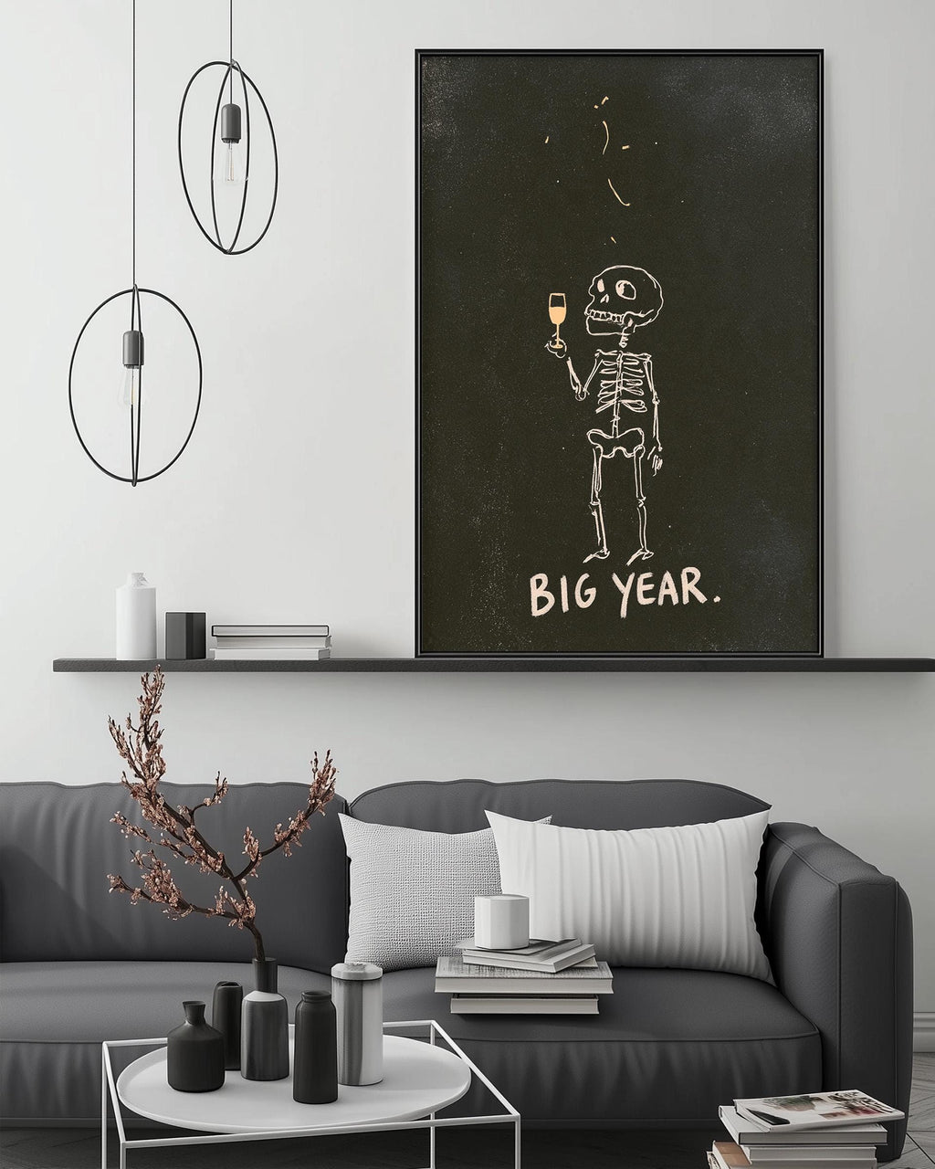 a living room with a gray sofa, a coffee table, and a large framed poster of a skeleton holding a wine glass. The poster has the text "BIG YEAR."