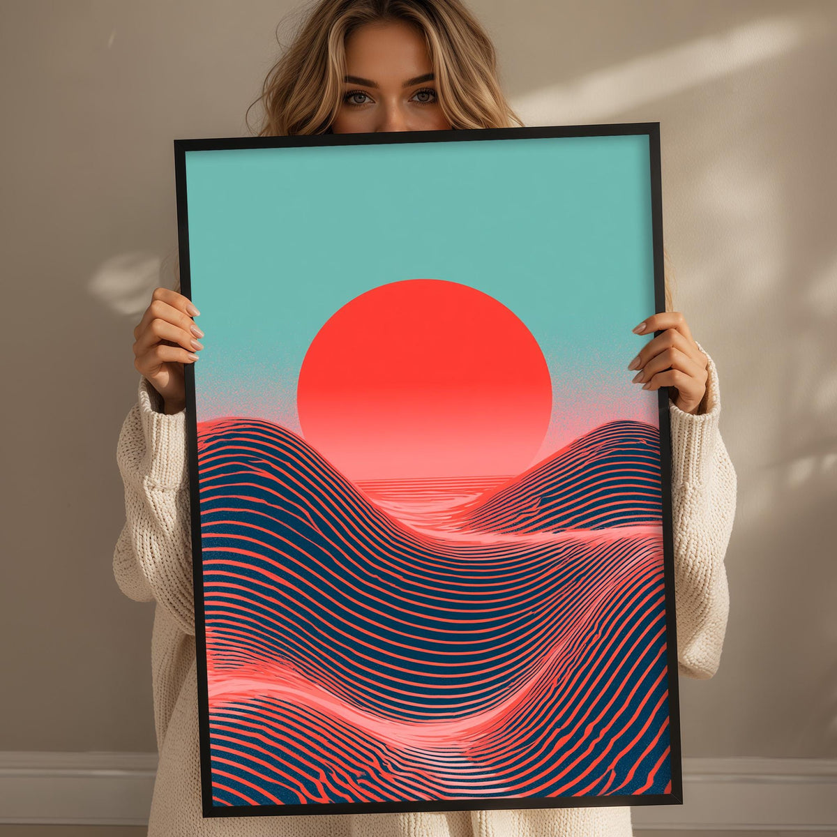 A woman is holding up a framed print of a vibrant sunset landscape with a large red sun and wavy lines across the sky.
