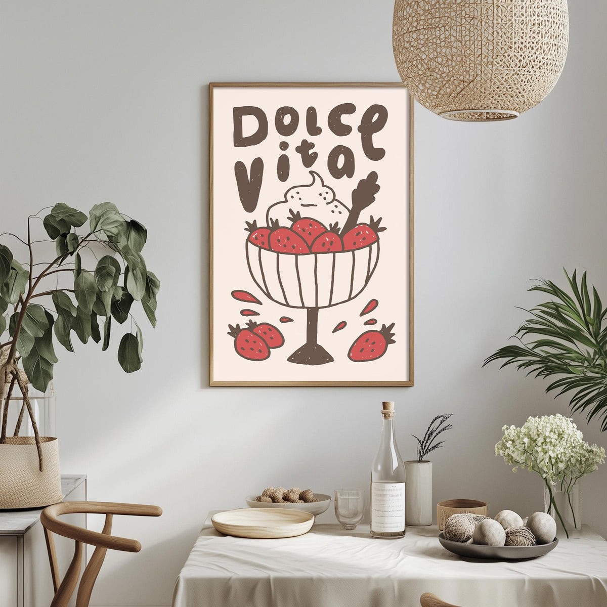 a dining table with a white tablecloth, a bowl of fruit, and a bottle of wine. Above the table, there is a framed poster with a drawing of a bowl of fruit and the text "Dolce Vita" written on it.
