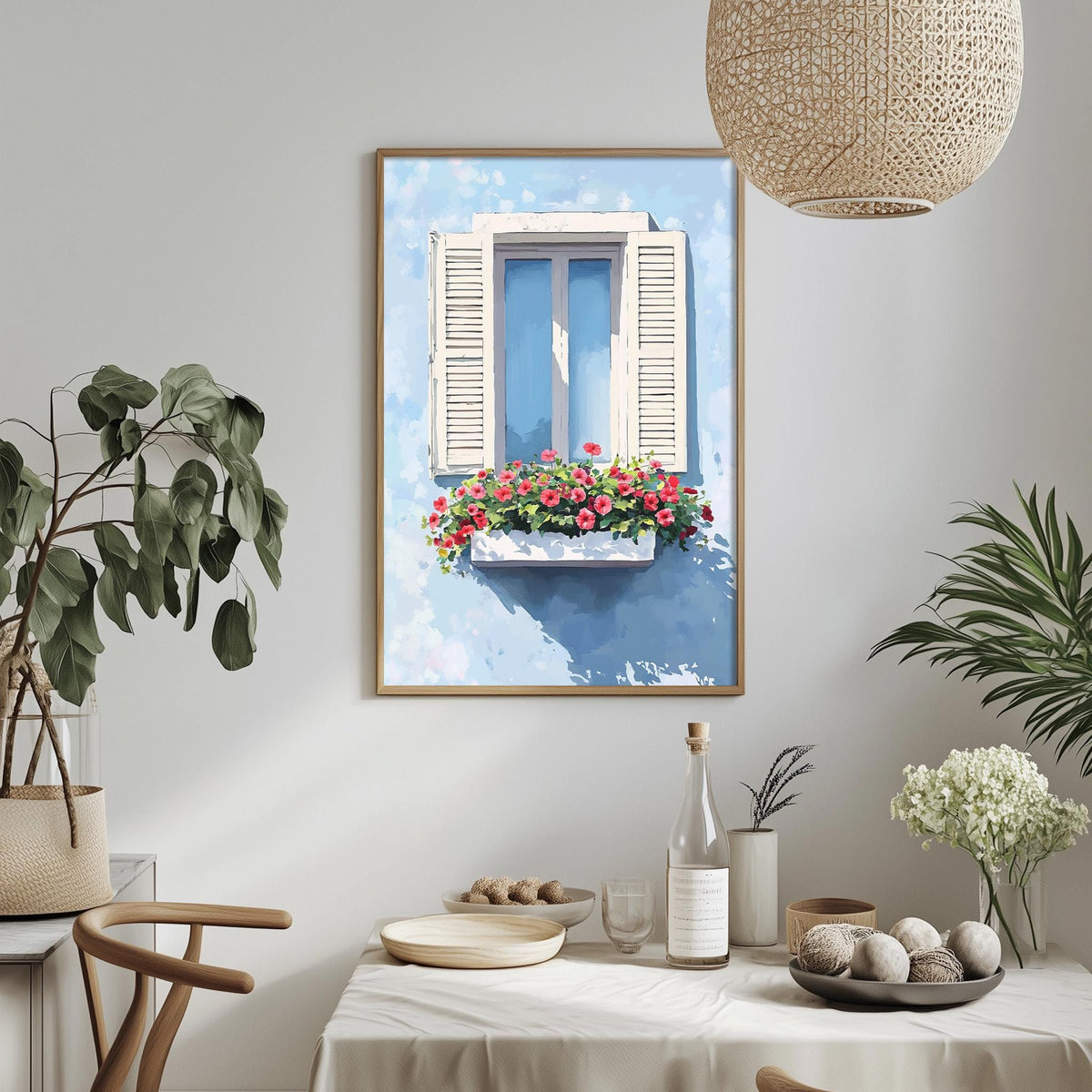 a dining table with a white tablecloth, a vase of white flowers, a bottle of wine, and a bowl of fruit. Above the table, there is a framed painting of a window with a flower box.