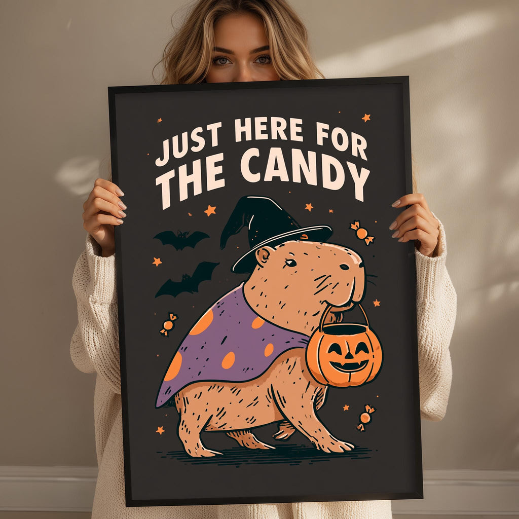 A woman is holding up a framed poster with a cartoon image of a beaver dressed as a witch, wearing a witch's hat and holding a carved pumpkin.